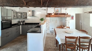 A kitchen with modern appliances, a dining area with a white table and chairs, and exposed wooden beams on the ceiling. - Nice home in Manthelan (Manthelan)