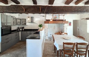 A kitchen with modern appliances, a dining area with a white table and chairs, and exposed wooden beams on the ceiling. - Nice home in Manthelan (Manthelan)