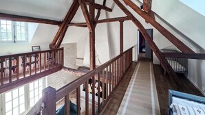 A high-ceilinged room with exposed wooden beams, a staircase with a wooden railing, and a view of a window. - Nice home in Manthelan (Manthelan)