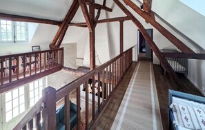 A high-ceilinged room with exposed wooden beams, a staircase with a wooden railing, and a view of a window. - Nice home in Manthelan (Manthelan)