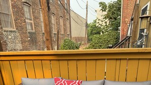Um sofá de vime com almofadas cinzas e uma almofada vermelha estampada em um deck de madeira.