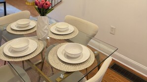Uma área de refeições com uma mesa de vidro posta para quatro pessoas, cercada por cadeiras brancas.