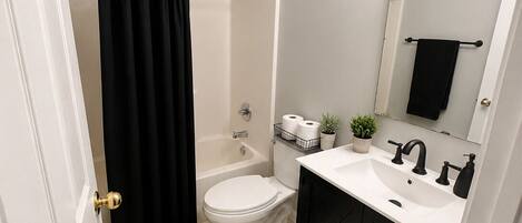 A bathroom with a bathtub, toilet, sink, and a mirror with lights.