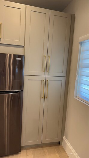 A kitchen with a stainless steel refrigerator, light-colored cabinets, and a window with blinds. - Cozy 1-BR 1-Bath house close to Beach in Naples, FL with A/C. (Naples)