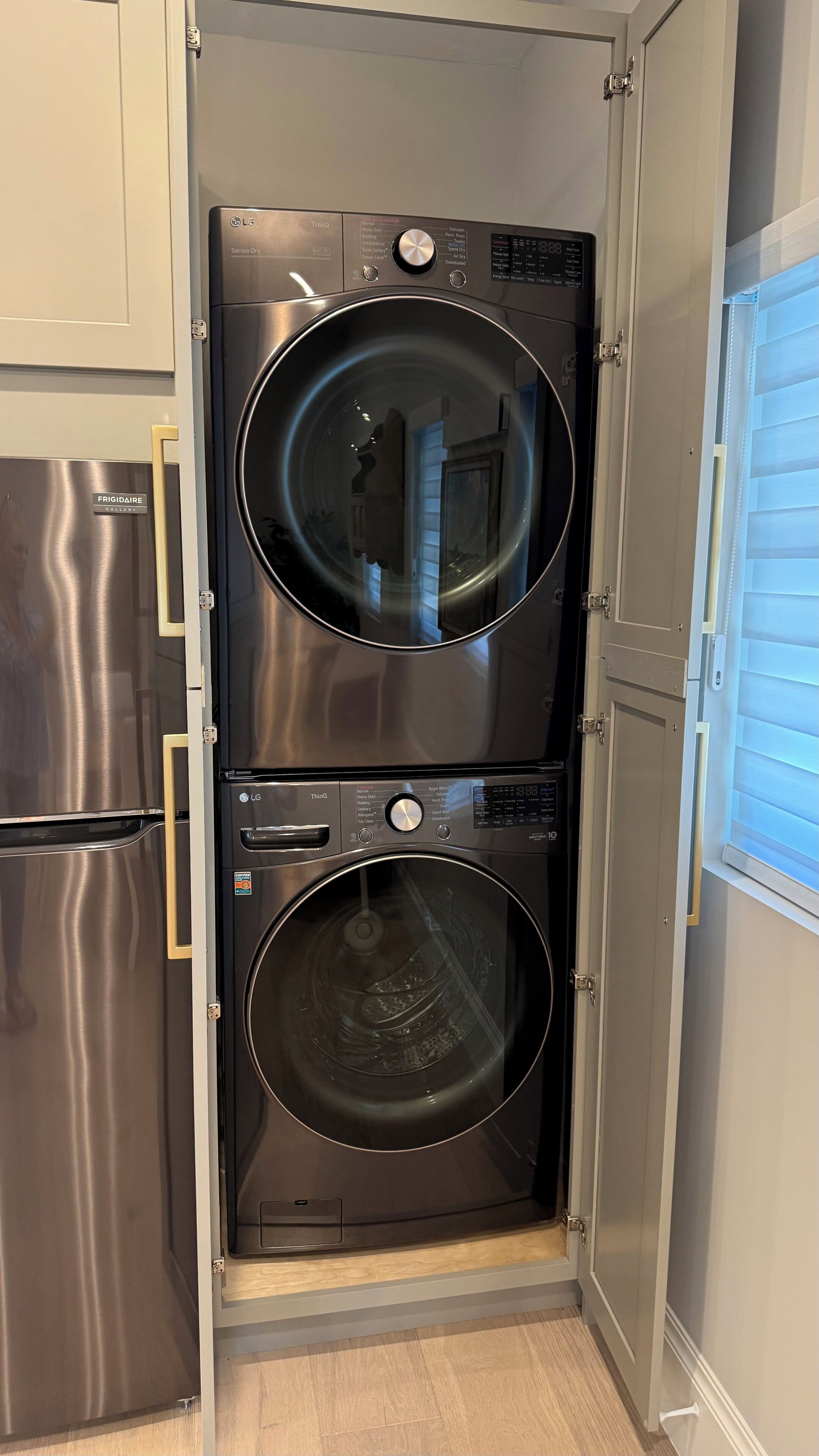 A compact laundry room with a stainless steel refrigerator and a double-door washer and dryer unit.