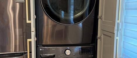 A compact laundry room with a stainless steel refrigerator and a double-door washer and dryer unit.
