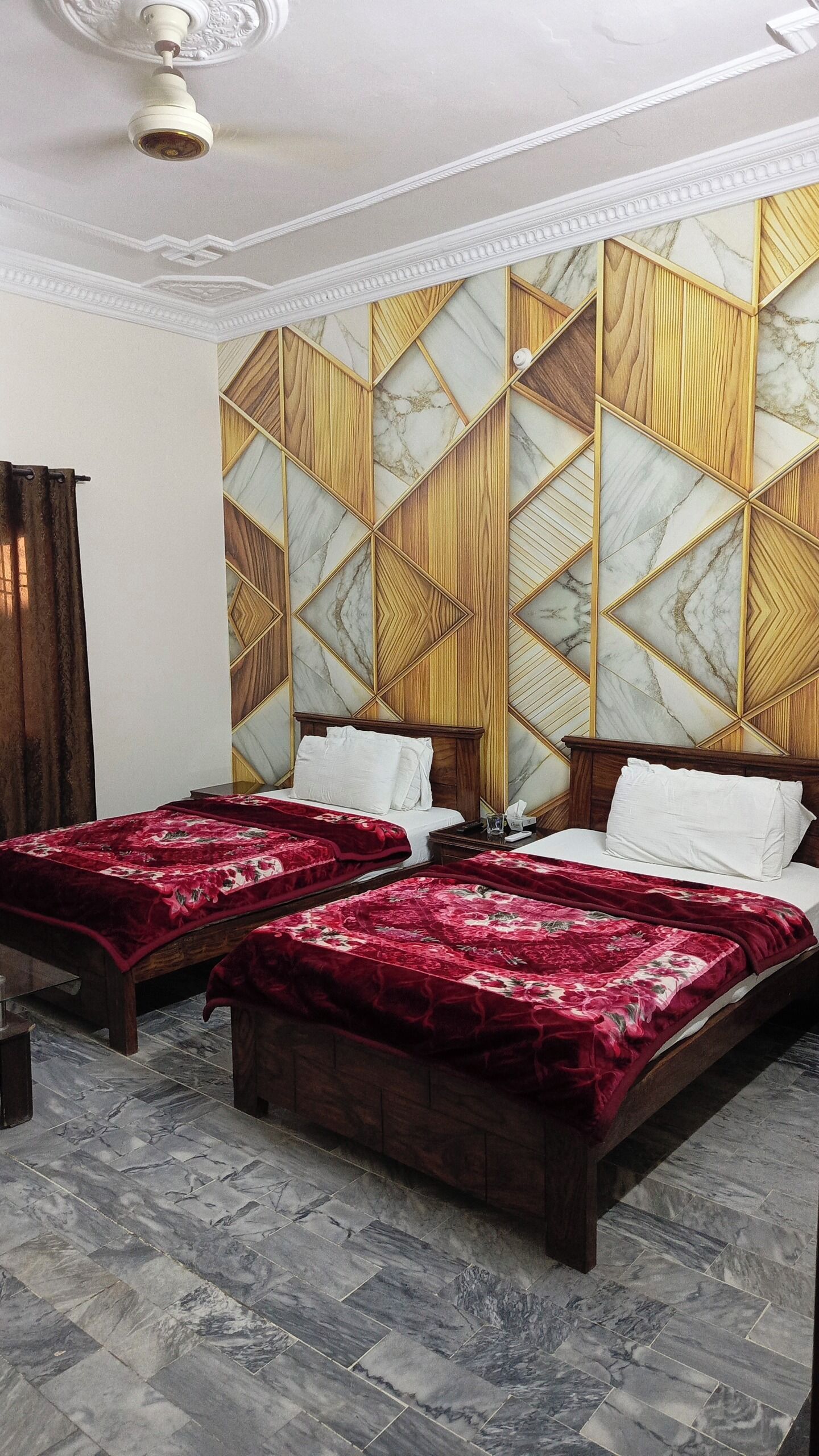 A hotel room with two beds, a marble-patterned wall, and a ceiling fan.