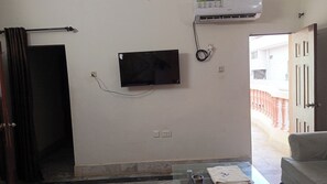 Ein Zimmer mit Flachbildfernseher an der Wand, einer Steckdose und einem Fenster mit Blick auf ein Gebäude.