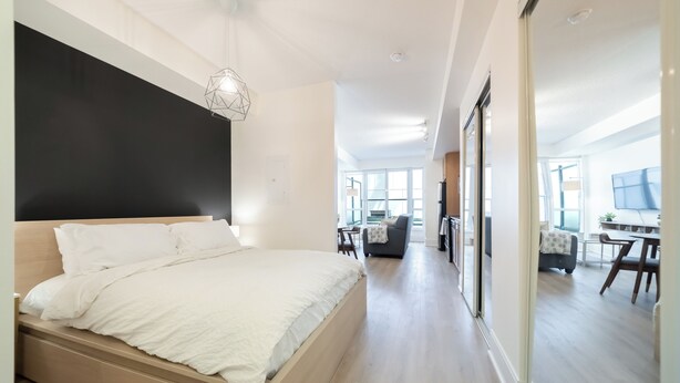 Una camera da letto moderna con un letto grande, una lampada a sospensione geometrica e vista sull'area soggiorno attraverso una porta in vetro.