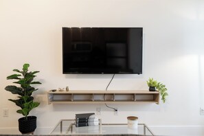 Ein Flachbildfernseher ist an einer Wand über einem hölzernen Regal montiert, auf dem ein Fernbedienung, Bücher und eine Kerze stehen.