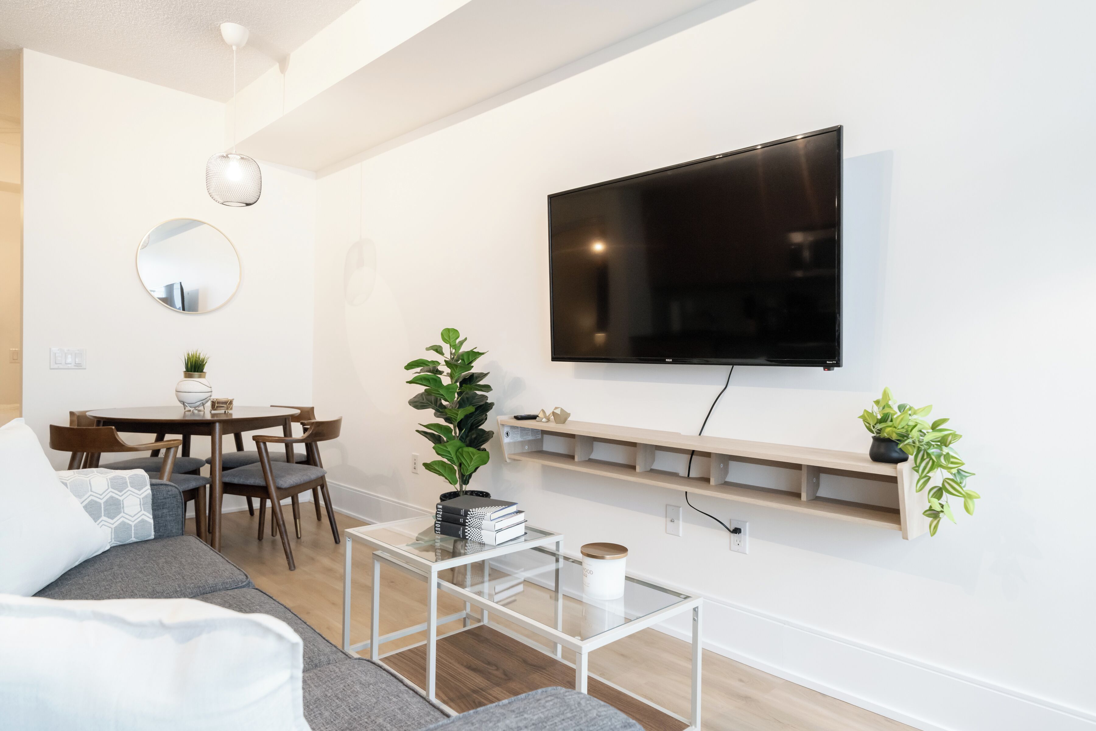 Ein modernes Wohnzimmer mit einem flachbildfernseher an der Wand, einem runden Spiegel, einem Esstisch mit Stühlen und einem Sofa.
