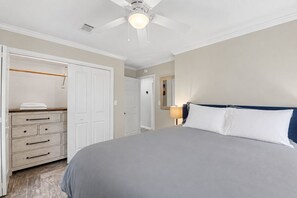 A bedroom with a bed, a wardrobe, a ceiling fan, and a nightstand with a lamp. - Ocean Springs Retreat, 5 min to downtown, Sleeps 8 (Ocean Springs)