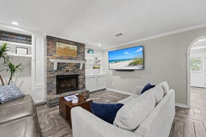 A living room with a fireplace, a television mounted on the wall, and a sofa. - Ocean Springs Retreat, 5 min to downtown, Sleeps 8 (Ocean Springs)