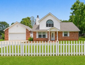 A two-story house with a garage, a front porch, and a picket fence. - Ocean Springs Retreat, 5 min to downtown, Sleeps 8 (Ocean Springs)
