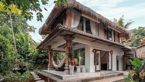 A traditional house with a thatched roof, a stone staircase, and a garden with a water feature. - Barong - one bedroom inspiring space (Gianyar)
