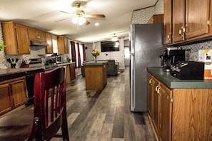 A kitchen with wooden cabinets, a refrigerator, a microwave, and a dining area with a chair. - Hidden Creek Guest Wing, Private 3BR Retreat Sleeps 10 (Huntsville)