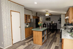 A kitchen with wooden cabinets, a central island, and a dining area with chairs. - Hidden Creek Guest Wing, Private 3BR Retreat Sleeps 10 (Huntsville)