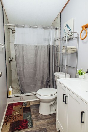 Ein Badezimmer mit Dusche, Toilette und einem weißen Waschbecken inklusive Spiegel.