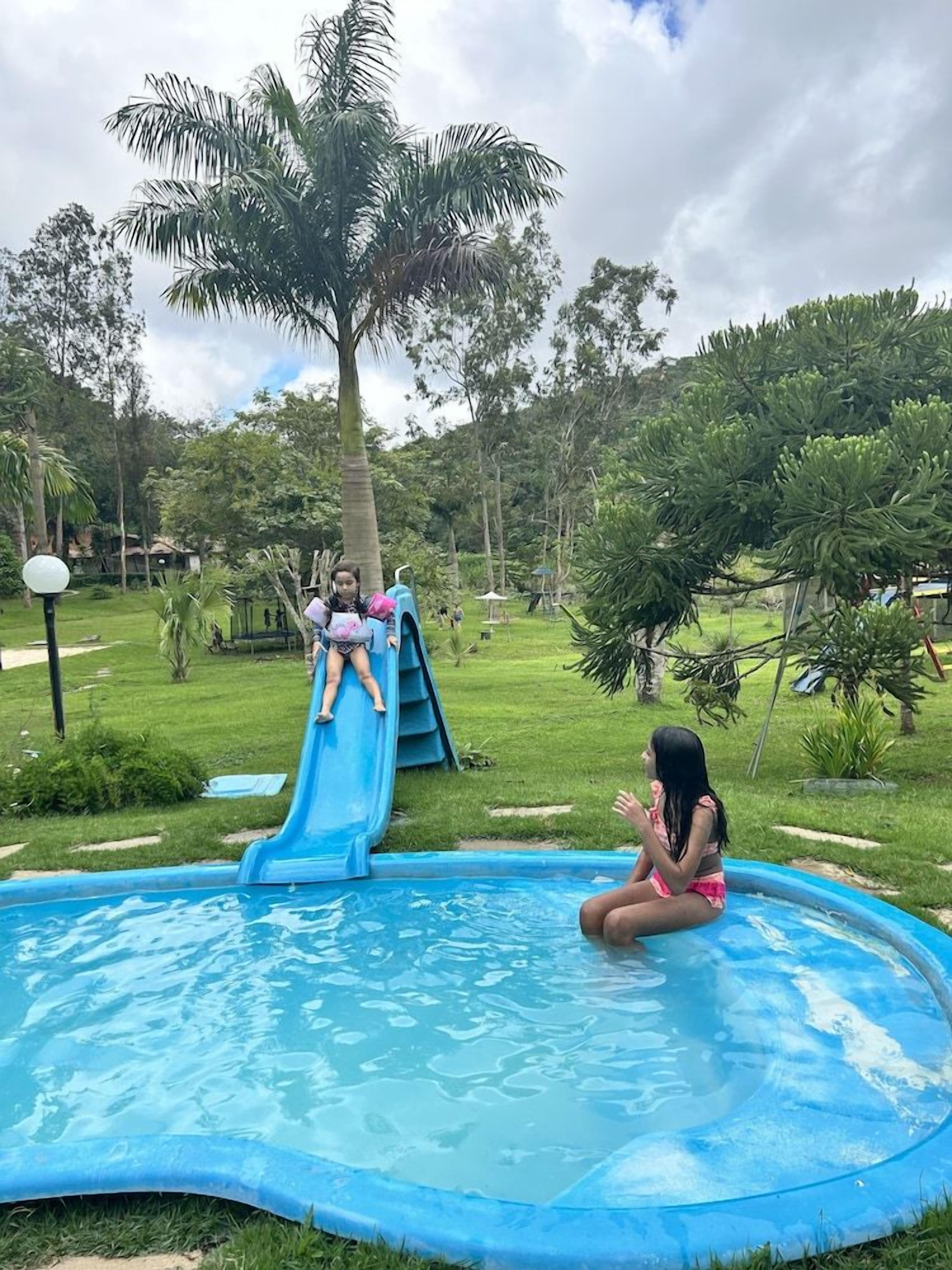 A swimming pool with a slide, surrounded by greenery and trees.