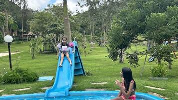 A swimming pool with a slide, surrounded by greenery and trees.