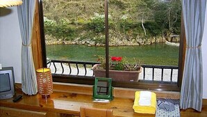 Una habitación con un escritorio de madera, televisor, lámpara y ventana con vista a un río y vegetación.