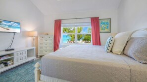 Un dormitorio con cama, cómoda, televisor y ventana con vista a la playa.