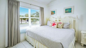 Ein Schlafzimmer mit einem Bett, Vorhängen, einem Fenster mit Jalousien und zwei gerahmten Bildern an der Wand.