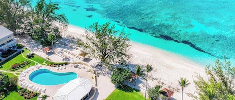 An aerial view of a resort with a swimming pool, beach, and clear turquoise waters.