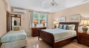 A bedroom with a bed, two bedside tables, a window with curtains, an air conditioning unit, and a ceiling fan. - Harbour Heights #19 Seven Mile Beach, 2 Bed, 2 Bath Ground Floor Condo (Seven Mile Beach)
