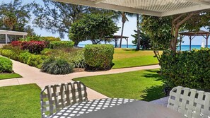 A patio area with a table and chairs, surrounded by well-maintained landscaping and a view of the ocean. - Harbour Heights #19 Seven Mile Beach, 2 Bed, 2 Bath Ground Floor Condo (Seven Mile Beach)