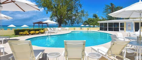 A pool area with lounge chairs and umbrellas, a lifeguard station, and a view of the ocean.