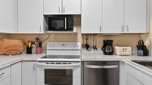 Una cocina con gabinetes blancos, microondas, estufa, lavavajillas, tostadora y varios utensilios.