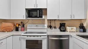 A kitchen with white cabinets, a microwave, a stove, a dishwasher, a toaster, and various utensils. - Harbour Heights #19 Seven Mile Beach, 2 Bed, 2 Bath Ground Floor Condo (Seven Mile Beach)