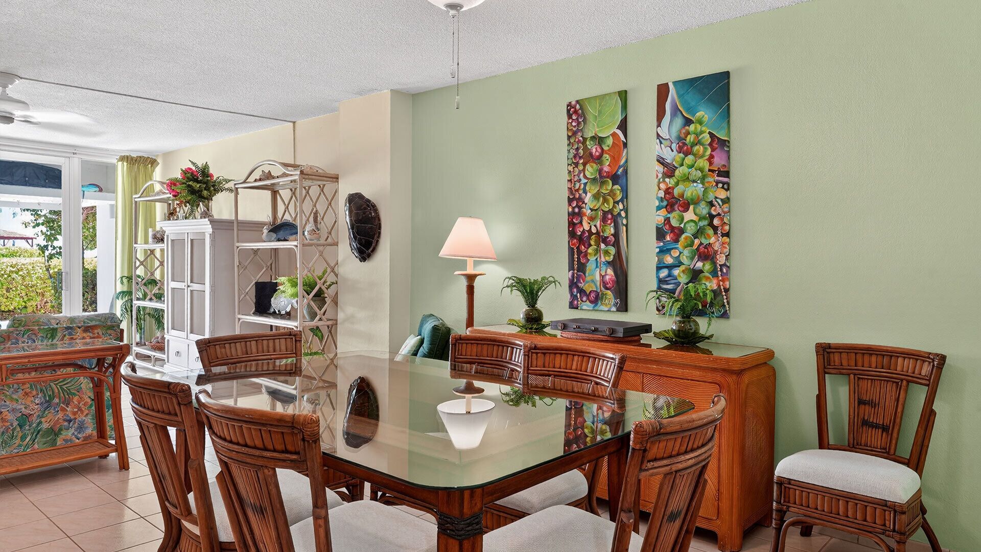Un coin repas avec une table en verre entourée de chaises en osier, un meuble blanc et deux tableaux accrochés au mur.