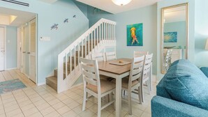 A dining area with a wooden table and chairs, a white staircase, and a blue wall with a painting. - Harbour Heights #26 Seven Mile Beach, 2 Bedroom, 2.5 Bathroom Second Floor Townhouse (Seven Mile Beach)