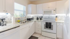 A modern kitchen with white cabinets, a stainless steel stove, a microwave, and a coffee maker. - Harbour Heights #26 Seven Mile Beach, 2 Bedroom, 2.5 Bathroom Second Floor Townhouse (Seven Mile Beach)