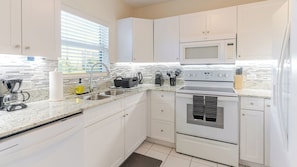 A modern kitchen with white cabinets, a stainless steel stove, a microwave, and a coffee maker. - Harbour Heights #26 Seven Mile Beach, 2 Bedroom, 2.5 Bathroom Second Floor Townhouse (Seven Mile Beach)