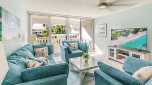 A living room with teal sofas, a glass coffee table, and a flat-screen TV. - Harbour Heights #26 Seven Mile Beach, 2 Bedroom, 2.5 Bathroom Second Floor Townhouse (Seven Mile Beach)