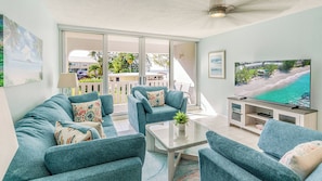 A living room with teal sofas, a glass coffee table, and a flat-screen TV. - Harbour Heights #26 Seven Mile Beach, 2 Bedroom, 2.5 Bathroom Second Floor Townhouse (Seven Mile Beach)