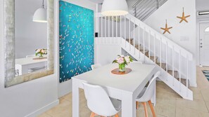 A modern interior with a white staircase, a dining area with a white table and chairs, and a teal wall with a boat pattern.