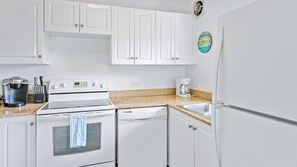 A kitchen with white cabinets, a stove, a dishwasher, and a coffee maker.
