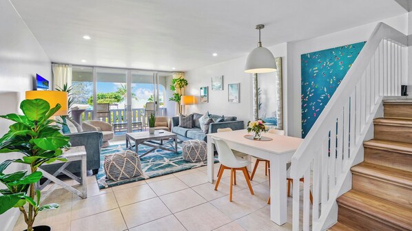 A modern living room with a dining area, a staircase, and a view of the outdoors.