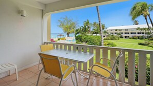 A balcony with a table and chairs, overlooking a pool and a building with a white roof. - Harbour Heights #8 Seven Mile Beach, 2 Bed, 2 Bath Second Floor Townhouse (Seven Mile Beach)