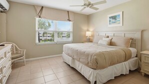 A bedroom with a bed, a chair, a nightstand, a ceiling fan, and a window with blinds. - Harbour Heights #8 Seven Mile Beach, 2 Bed, 2 Bath Second Floor Townhouse (Seven Mile Beach)
