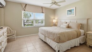 A bedroom with a bed, a chair, a nightstand, a ceiling fan, and a window with blinds. - Harbour Heights #8 Seven Mile Beach, 2 Bed, 2 Bath Second Floor Townhouse (Seven Mile Beach)