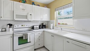 A kitchen with white cabinets, a microwave, a stove, a toaster, a coffee maker, and a window with a view of greenery. - Harbour Heights #8 Seven Mile Beach, 2 Bed, 2 Bath Second Floor Townhouse (Seven Mile Beach)