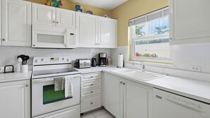 A kitchen with white cabinets, a microwave, a stove, a toaster, a coffee maker, and a window with a view of greenery. - Harbour Heights #8 Seven Mile Beach, 2 Bed, 2 Bath Second Floor Townhouse (Seven Mile Beach)