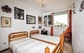 A bedroom with two wooden beds, a window with a view of buildings, and various framed artworks on the wall. - 5 bedroom cozy home in Sainte Marie La Mer Pl (Sainte Marie La Mer Pl)