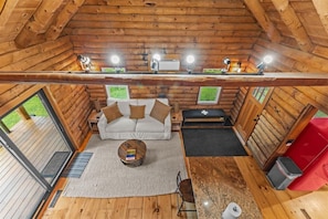 Interior de una cabaña de troncos con un sofá, una mesa de centro y una ventana.