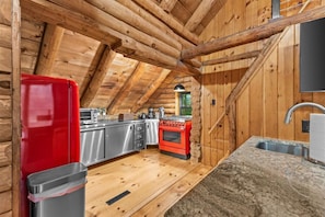 Cocina de cabaña de madera con techo de madera, estufa roja, electrodomésticos de acero inoxidable y encimera de granito.